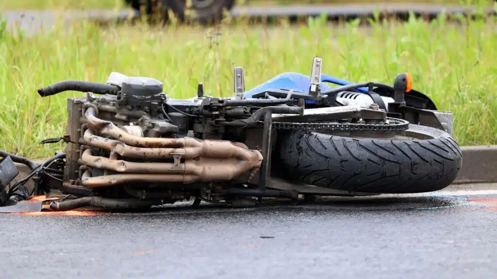 A motorcycle lying on its side on the road, surrounded by grass, depicting the aftermath of an accident.